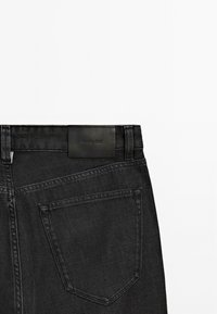 Jeans neri in denim con una finitura testurizzata, caratterizzati da un'etichetta in pelle sulla vita e una tasca posteriore con una cucitura. 