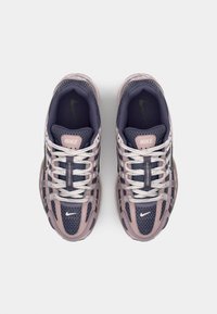 Baskets Nike avec une tige en maille bleu marine et rose clair, dotées de lacets blancs et d'un logo vert, affichant un design épuré.