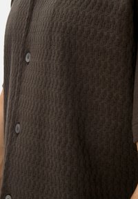 Brown textured button-up shirt featuring a geometric pattern, with prominently visible buttons and a soft, woven fabric design.