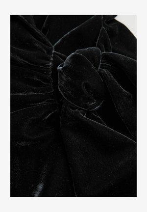 Melnās samta audums ar savāktiem laukumiem un mezglotu dekoratīvu detaļu. Mīksta tekstūra un bagāta krāsa, ar viegli spīdīgu virsmu.