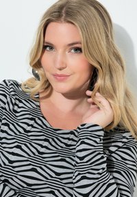 Dlouhý rukáv, šedý top s černým vzorem zebřích pruhů. Kulatý výstřih a volný střih. Texturovaný povrch s měkkým materiálem.