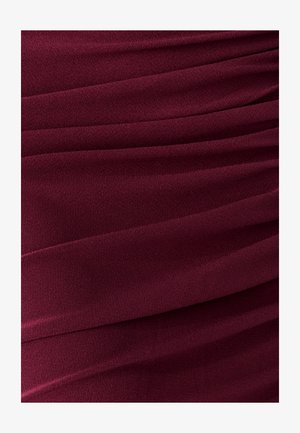 Tissu bordeaux avec une texture douce et fluide présentant des plis diagonaux. Le matériau semble léger et lisse avec un éclat subtil.