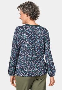 Langarmbluse in Dunkelblau mit einem bunten abstrakten Muster, mit elastischen Bündchen und einem rundem Ausschnitt.