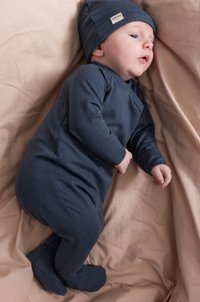 Námornícky modrý bavlnený overal s ladiacou čiapkou, s dlhými rukávmi, nožným dizajnom a mäkkou textúrou, položený na svetlom béžovom pozadí.
