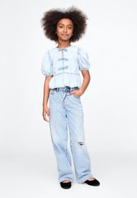Lyseblå denim-topp med puffermer, dekorert med knapper og peplum i livet, kombinert med vide, lyseblå jeans.