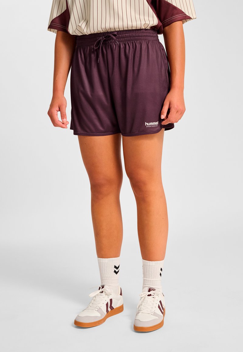 Mörklila atletshorts med resår i midjan och dragsko. Kombinerade med vita sneakers och krämfärgade strumpor med ett mörkt mönster.