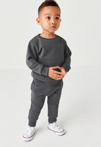 Grauer Baumwoll-Sweatshirt und Jogginghose mit Rippbündchen, kombiniert mit weißen Sneakers mit roten Akzenten. Einfaches, komfortables Design für Kinder.