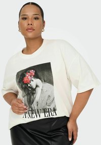 Camiseta color crema con un gran gráfico en blanco y negro de una mujer con acentos florales. Manga corta y corte relajado. Pantalones de cuero sintético negro.