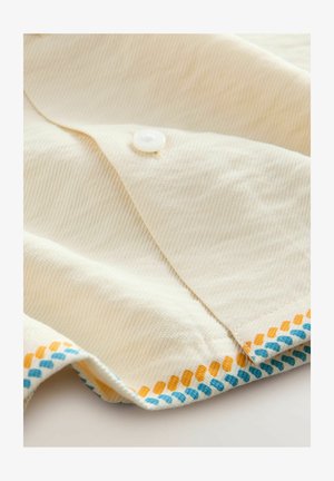 Világos krémszínű, gombos ing texturált anyagból; díszítő kék és narancssárga varrással ellátott szegéllyel a hemnél.