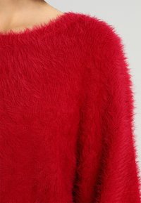 Czerwony, puszysty sweter z szerokim dekoltem i luźnym krojem, o miękkiej, teksturowanej powierzchni podkreślającej żywy kolor.