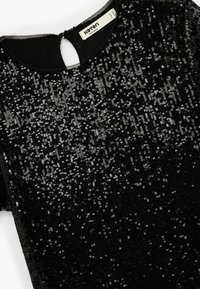 Czarna sukienka krótko rękawowa z okrągłym dekoltem, z teksturowaną powierzchnią ozdobioną ćwiekami w różnych rozmiarach, podkreślająca szczegół z wycięciem na plecach.