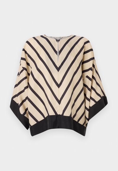 Beige bluse med sterke svarte chevron-striper, brede ermer og svart kant, med V-hals og baklukking. Glatt stofftekstur.