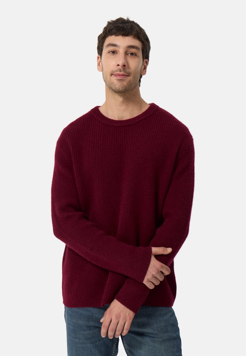 Burgunderfärgad stickad tröja med ribbad textur, rund halsringning och långa ärmar, kombinerad med blå denimjeans.