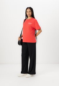 Camiseta roja con el texto "MAMA", de corte holgado. Combinada con pantalones de pierna ancha negros y zapatillas blancas. Textura de rayas en los pantalones.