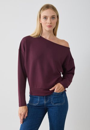 Burgunderfarget avskåret sweatshirt med lange ermer og en avslappet passform, kombinert med mørkeblå jeans, med en glatt tekstur.