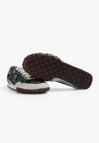 Sneakers z teksturowaną cholewką w czarno-białe paski, szarym zamszowym czubkiem i brązową gumową podeszwą z wyraźnymi wypustkami zapewniającymi dobrą przyczepność.