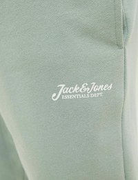 Lichtgroene sweatshirtstof met gestructureerde brei, met een witte gedrukte logo waarop staat "Jack & Jones Essentials Dept." in cursiefschrift.