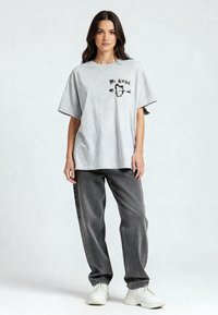 T-shirt gris oversize avec le texte "Mi Amor" et un graphique de cœur. Associé à un pantalon ample gris et des baskets blanches. Texture de tissu plate.