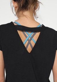 Czarna koszulka sportowa z głębokim wycięciem V z tyłu, z krzyżującymi się ramiączkami w odcieniach niebieskiego i szarego, wykonana z lekkiego, oddychającego materiału.