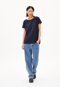 Navyblauwe katoenen T-shirt met opgerolde mouwen, gecombineerd met lichtblauwe denimjeans. De look wordt afgemaakt met zwarte klompen. Eenvoudig ontwerp.