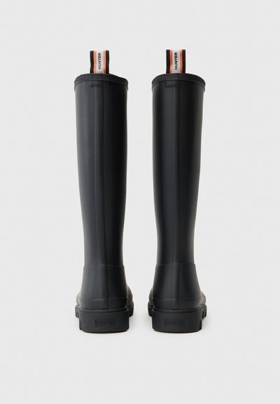 Par čizama od crne gume velikih pružanja s logotipima na vrhu i nazivom brenda utisnutim na peti, viđeno sa stražnje strane.