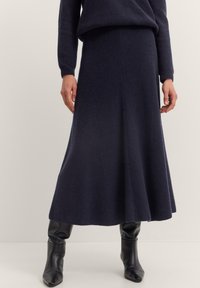 Marineblaue Strickrock mit gerippter Textur, ausgestelltem Design, bis zur Mitte der Wade reichend, kombiniert mit knielangen schwarzen Lederstiefeln.