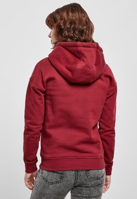 Sudadera con capucha de color burdeos, con una capucha grande, tela suave y puños acanalados. La vista trasera muestra un diseño simple sin patrones ni acentos adicionales.