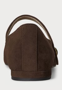 Brown suede shoe with a low heel, featuring a curved back and a strap across the top. Smooth texture with a plain design and minimal hardware.