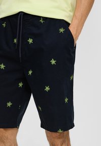 Marineblau Shorts aus einem Stoff mit grüner Blätterstickerei, mit elastischem Bund und seitlichen Taschen. Strukturierter, lässiger Schnitt.
