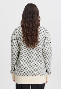 Maglione a maglia crema con motivi a diamante neri, con ampi polsini e orlo a coste. Il tessuto sembra morbido e testurizzato.