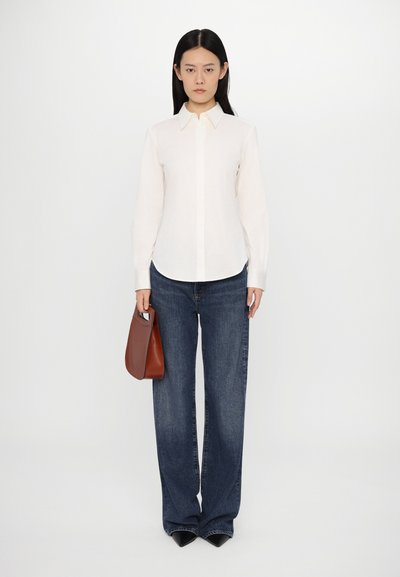 White button-up shirt with a collar, paired with dark blue wide-leg jeans. The model holds a small brown handbag.