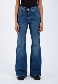 Flared blue denim jeans with high waist, contrasting stitching, and five-pocket design. The fabric has a slight fade and soft texture.