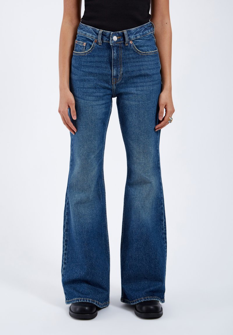 Flared blue denim jeans with high waist, contrasting stitching, and five-pocket design. The fabric has a slight fade and soft texture.