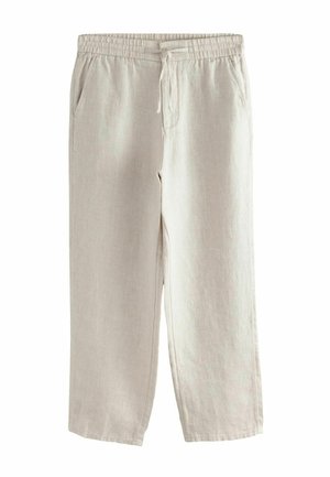 Bézs texturált nadrág hátsó foltzsebbel és rugalmas derékpánttal, sötét bőrtónusú személy által fehér inggel viselve.