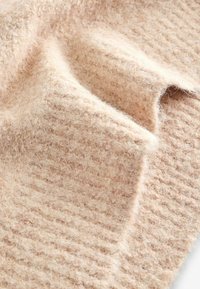 Zachte, gestructureerde stof in lichtbeige, met een geribbelde patroon en een fuzzy oppervlak. Het materiaal lijkt warm en uitnodigend.