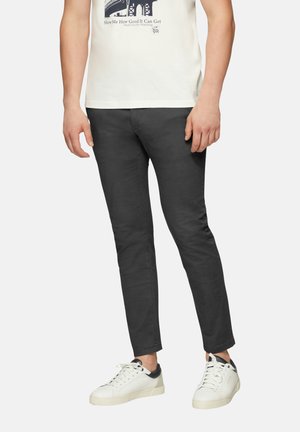 Szare slim-fit chinos wykonane z miękkiej bawełny. Noszone z białą koszulką z grafiką i białymi sneakersami z granatowymi akcentami.