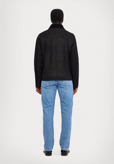 Schwarze Wildlederjacke mit hohem Kragen, schlichter Rückseite und kontrastierenden hellblauen Jeans. Flache, glatte Textur, einfaches Design, keine sichtbaren Beschläge.