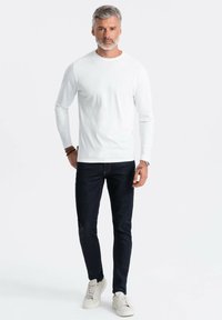 Weißes Langarmhemd, dunkle Jeans und helle Sneaker. Minimalistisches Design mit schlanker Passform und glatter Textur. Keine Muster oder Akzente.