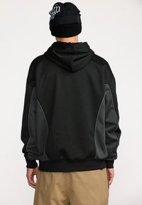 Hoodie noir avec accents gris sur les côtés et coutures contrastantes. Tissu doux, coupe décontractée, doté d'une capuche et de poignets côtelés.