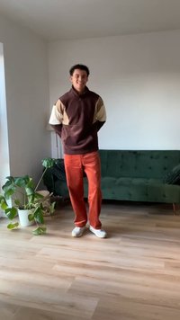 Μπράουν και μπεζ χρώμα-μπλοκαρισμένη μπλούζα με ψηλό γιακά, σε συνδυασμό με φωτεινές πορτοκαλί παντελόνες από χοντρούς καμβά και λευκά αθλητικά παπούτσια. Εσωτερικός χώρος.