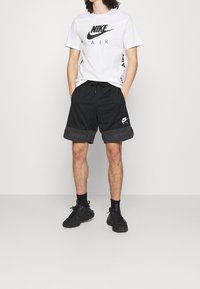 Černé šortky Nike s texturovaným designem, se stahovací šňůrkou, šedým okrajem a bílým logem. Doplněno o bílý tričko s krátkým rukávem od Nike.