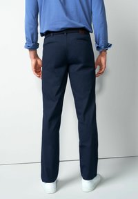 Marineblauwe broek met een subtiel ruitpatroon, slim fit en riemlussen, gecombineerd met witte sneakers en een blauw overhemd met lange mouwen.