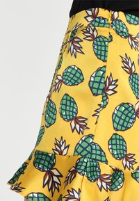 Jupe jaune avec un motif d'ananas en vert et marron, avec un ourlet volants et une fermeture éclair sur le côté. Texture de tissu lisse.