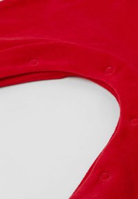 Tissu en velours rouge avec une texture douce, présentant un col rond et des boutons-pression le long du bord. Fini propre et lisse.