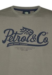 Oliven grøn bomuld t-shirt med et blåt grafisk tryk, der står "Petrol & Co. Denim Driven Workwear" med et ternet flag detalje.