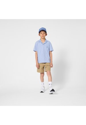 Vaaleansininen lyhythihainen poolopaita timanttikuvioisena, beiget shortsit, valkoiset sukat ja lenkkarit, joissa mustia yksityiskohtia, sekä sininen lippalakki.