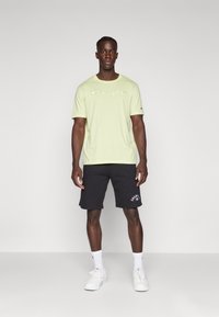 Ljusgrön kortärmad t-shirt med "Champion"-logotyp, matchad med svarta shorts med logotypdetaljer. Vita sneakers och ankelsockor fulländar outfiten.
