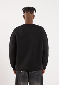 Svart oversized sweatshirt med rund hals og lange ermer, laget av et mykt materiale, kombinert med slitte grå jeans.