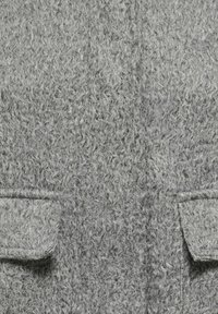 Manteau en laine grise à texture irrégulière, doté de deux poches avant et d'une coupe structurée. Le tissu présente une légère brillance et une sensation de chaleur.