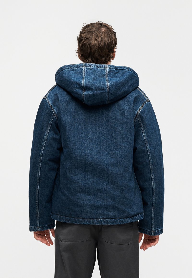 Denimjakke i mørkeblå med hætte, med markante sømme, en afslappet pasform og en tekstureret finish. Flad kant og oversized silhuet.
